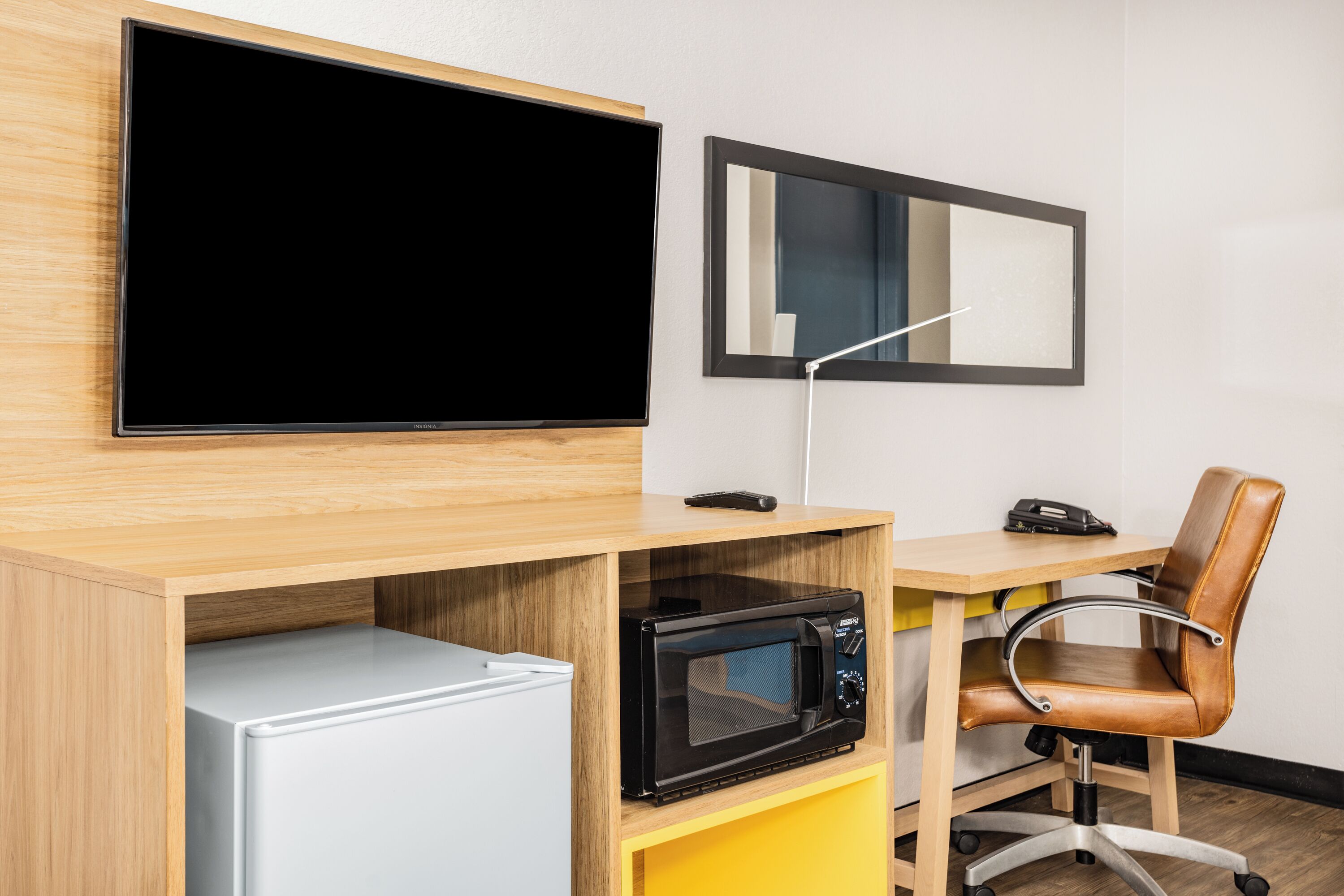 A compact office space with a flat-screen TV, a microwave, a refrigerator, a desk, and a chair.