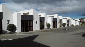 Fila de habitaciones de hotel numeradas con diseño moderno, un estacionamiento y cielo despejado.