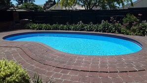 Una piscina de borde curvo, rodeada por un patio de ladrillo.