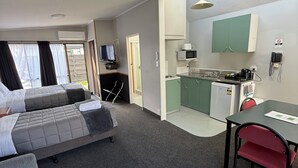Una habitación de hotel con dos camas, un kitchenette, una mesa de comedor y un televisor.