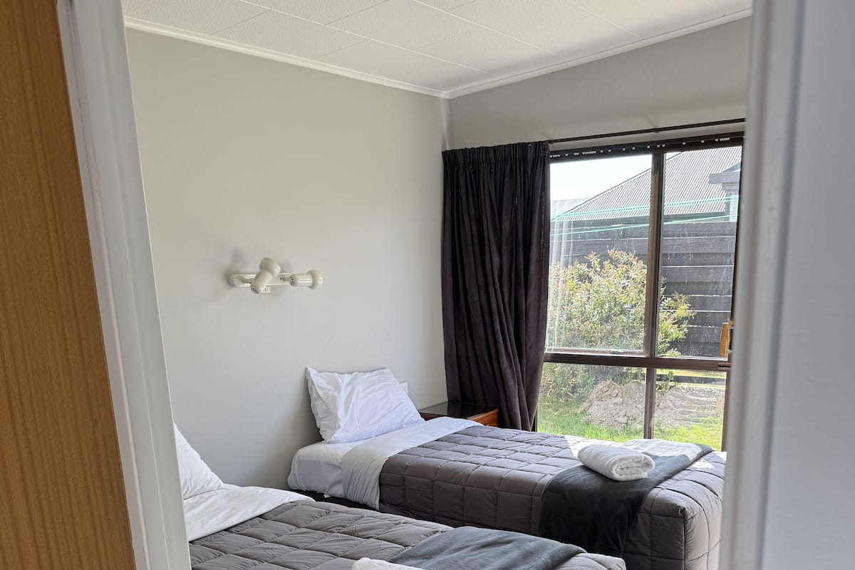 A hotel room with two beds, a large window, and a view of the outside.