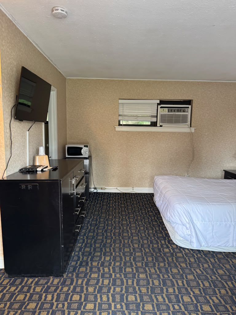 Een hotelkamer met een bed, een bureau met een magnetron, een televisie en een ventilatie rooster.