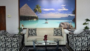A room with a large tropical-themed mural, a sofa, two patterned armchairs, and a glass coffee table. - Atlantic Inn & Suites (Belmar)
