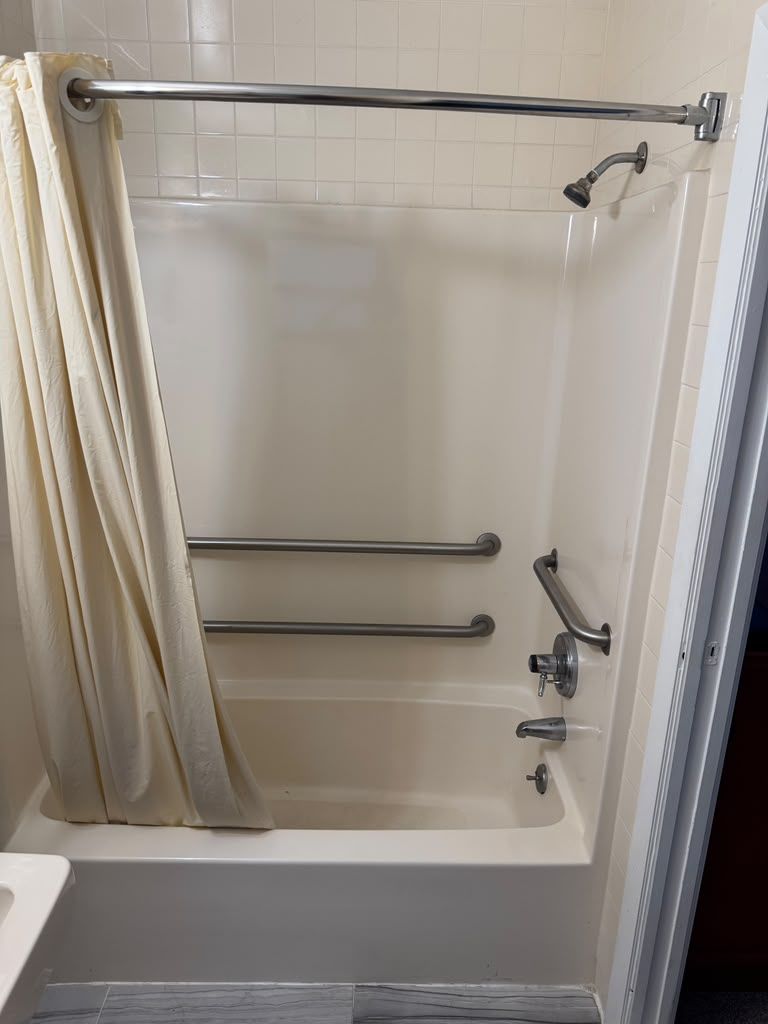 Una ducha con puerta de vidrio, una barra de apoyo de metal y una cortina.