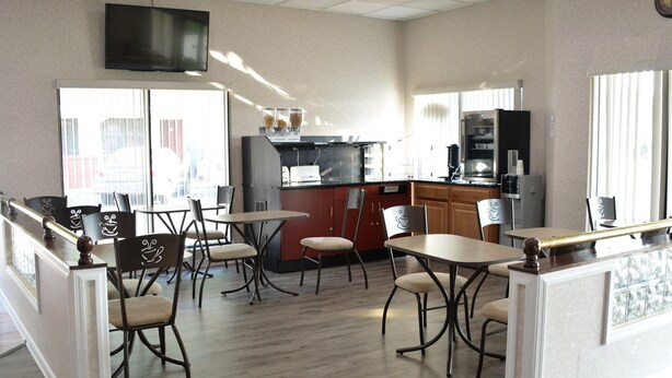 A restaurant with a counter, tables, chairs, a television, and a kitchen area. - Atlantic Inn & Suites (Belmar)