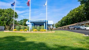 A motel with a blue exterior, two flagpoles with flags, and a well-maintained lawn. - Atlantic Inn & Suites (Belmar)