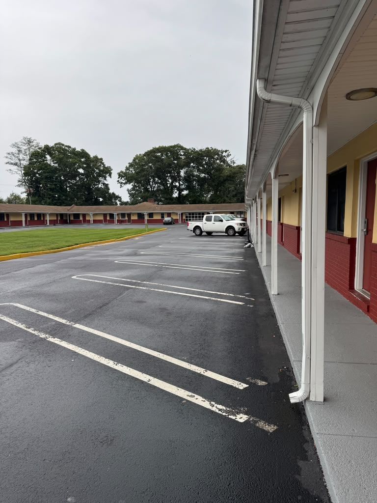 A parking lot with marked spaces, a building with a red and yellow facade, and a white vehicle parked in the distance.