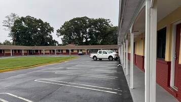 A parking lot with marked spaces, a building with a red and yellow facade, and a white vehicle parked in the distance.