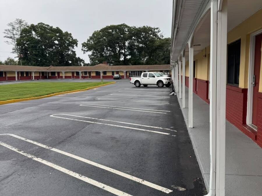 A parking lot with marked spaces, a building with a red and yellow facade, and a white vehicle parked in the distance.