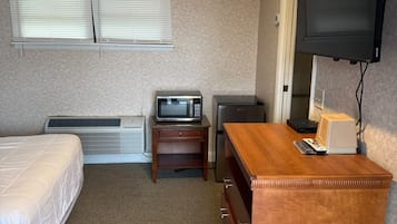 A hotel room with a bed, a desk, a television, and a heater.