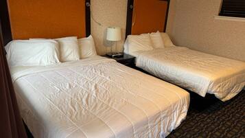 A hotel room with two beds, a nightstand with a lamp, and a window with blinds.