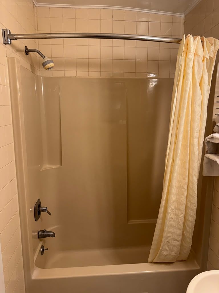 A shower with a glass door, a metal showerhead, and a beige curtain.