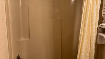A shower with a glass door, a metal showerhead, and a beige curtain.
