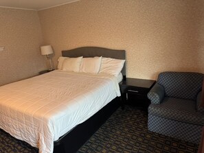 Una habitación de hotel con cama, mesita de noche, lámpara y un sillón estampado.