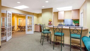 A hotel room with a kitchenette, a dining area with chairs, and a large window.
