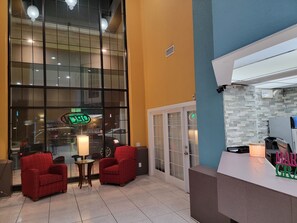 A hotel lobby with two red armchairs, a reception desk, and a large window with a neon sign. - Extend-a-Suites - Extended Stay, I-40 Amarillo West (Amarillo)