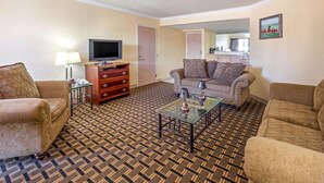 A hotel room with a patterned carpet, two sofas, a coffee table, a TV, and a dresser.