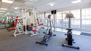 A gym with various exercise machines, large windows, and a mirrored wall.
