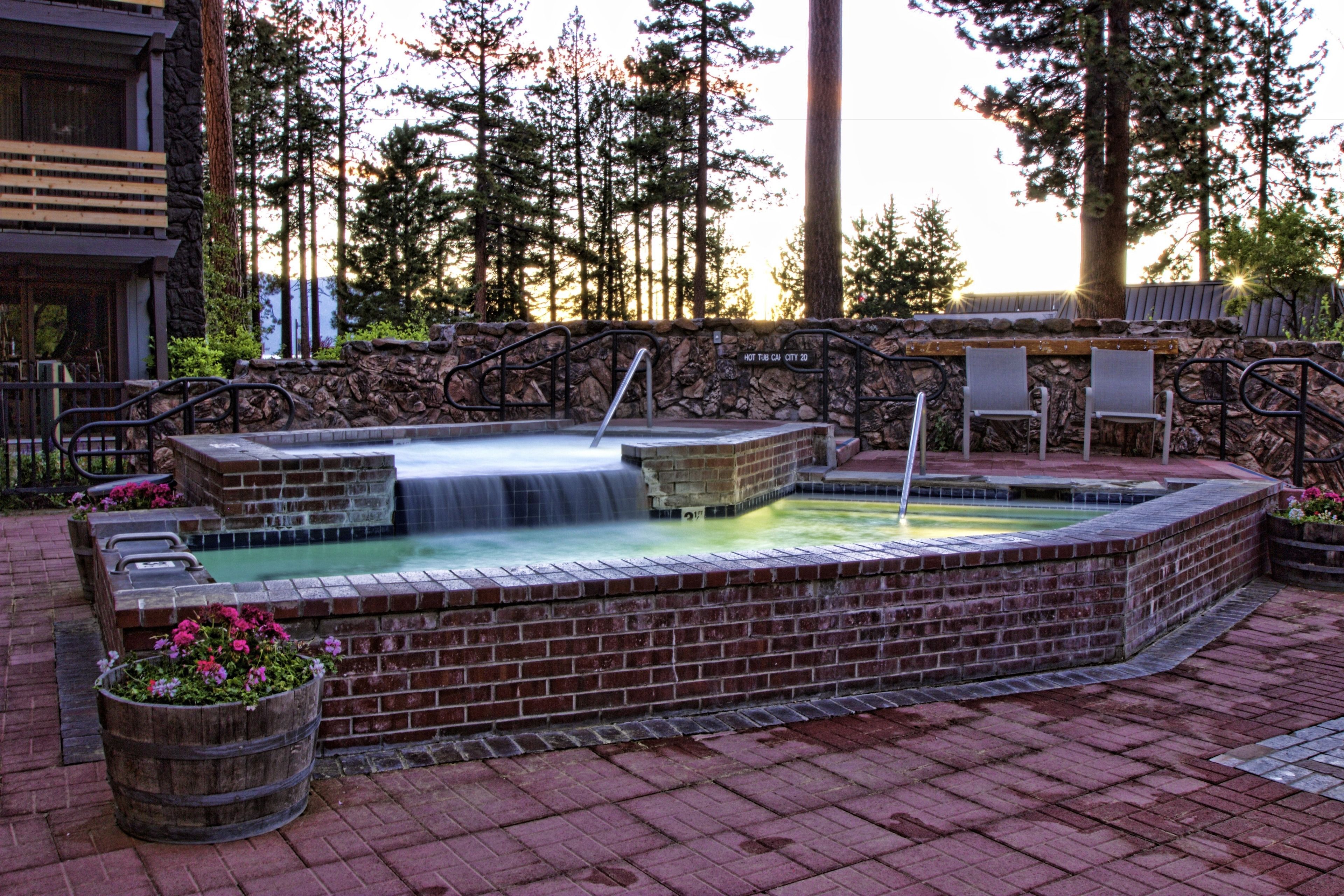 A hot tub area with a stone wall, wooden benches, and a waterfall feature.