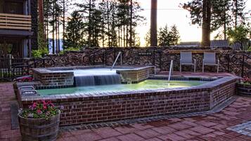 A hot tub area with a stone wall, wooden benches, and a waterfall feature.