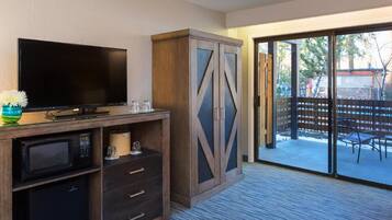 Quarto de hotel com televisão de tela plana, armário de madeira com gavetas, micro-ondas e porta de vidro deslizante que dá para uma área externa com varanda e mobiliário.