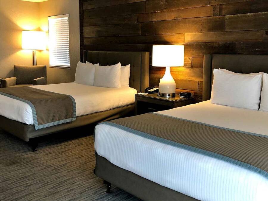 A hotel room with two beds, a small table, and two bedside lamps.