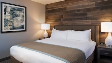 Ein Hotelzimmer mit einem großen Bett, zwei Nachttischen mit Lampen, einem hölzernen Kopfteil und einem gerahmten, abstrakten Gemälde an der Wand.