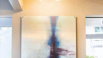 A bar area with a wooden ceiling, a hanging light fixture, a large abstract painting, and two bar stools with blue cloths.