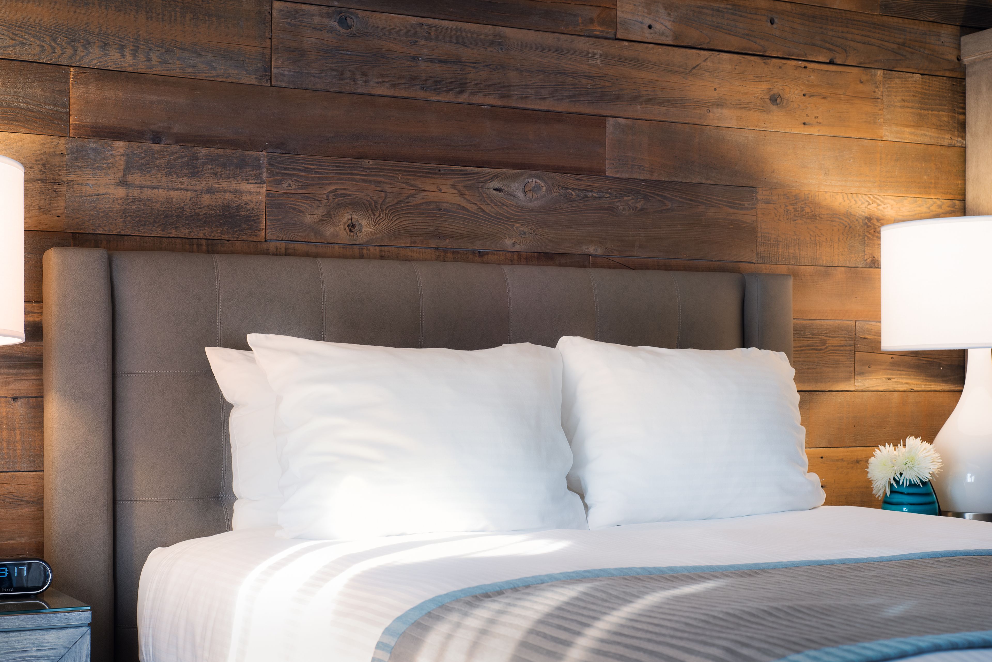 A neatly made bed with white linens and a grey headboard, set against a wooden wall.