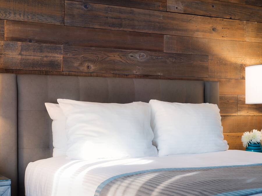 A neatly made bed with white linens and a grey headboard, set against a wooden wall.