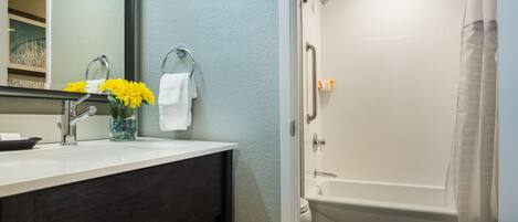 A bathroom with a sink, mirror, and a shower with a curved tub.