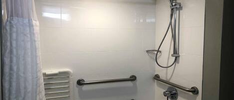 A modern bathroom with white tiles, a shower with a handheld hose, and two grab bars for support.