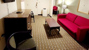 A room with a TV mounted on the wall, a red sofa, a patterned carpet, a wooden table, and a chair. - Town Inn (Bordentown)