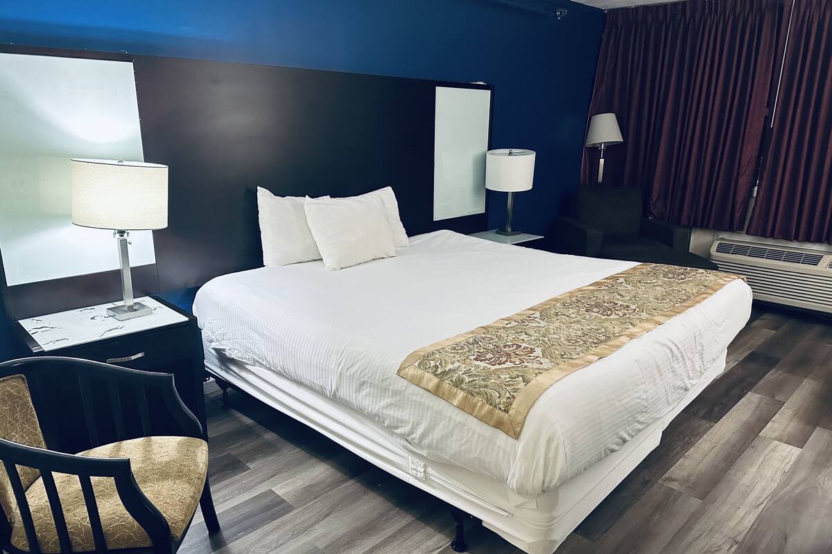A hotel room with a large bed, two bedside lamps, a desk with a chair, a mirror, and a window with curtains.
