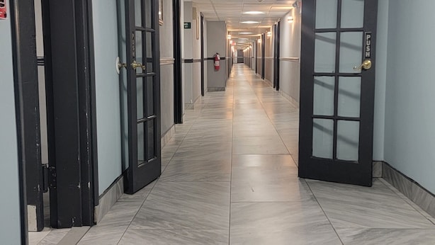 A long, narrow hotel corridor with doors on both sides, a tiled floor, and overhead fluorescent lighting. - Town Inn (Bordentown)