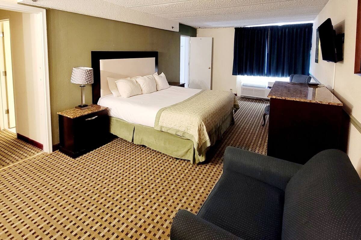 A hotel room with a bed, a desk, a chair, and a patterned carpet.
