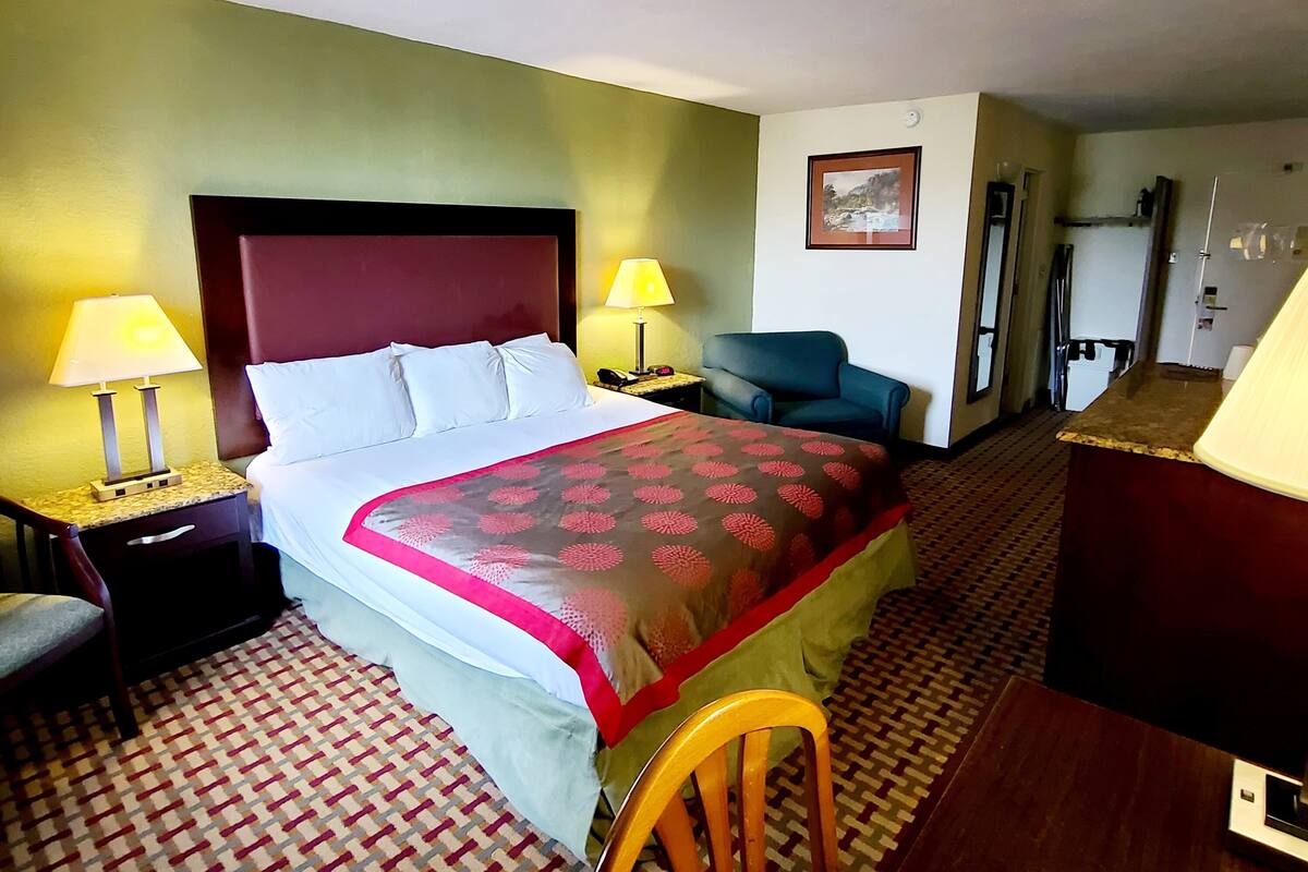 A hotel room with a bed, two bedside tables with lamps, a chair, a desk, and a door.