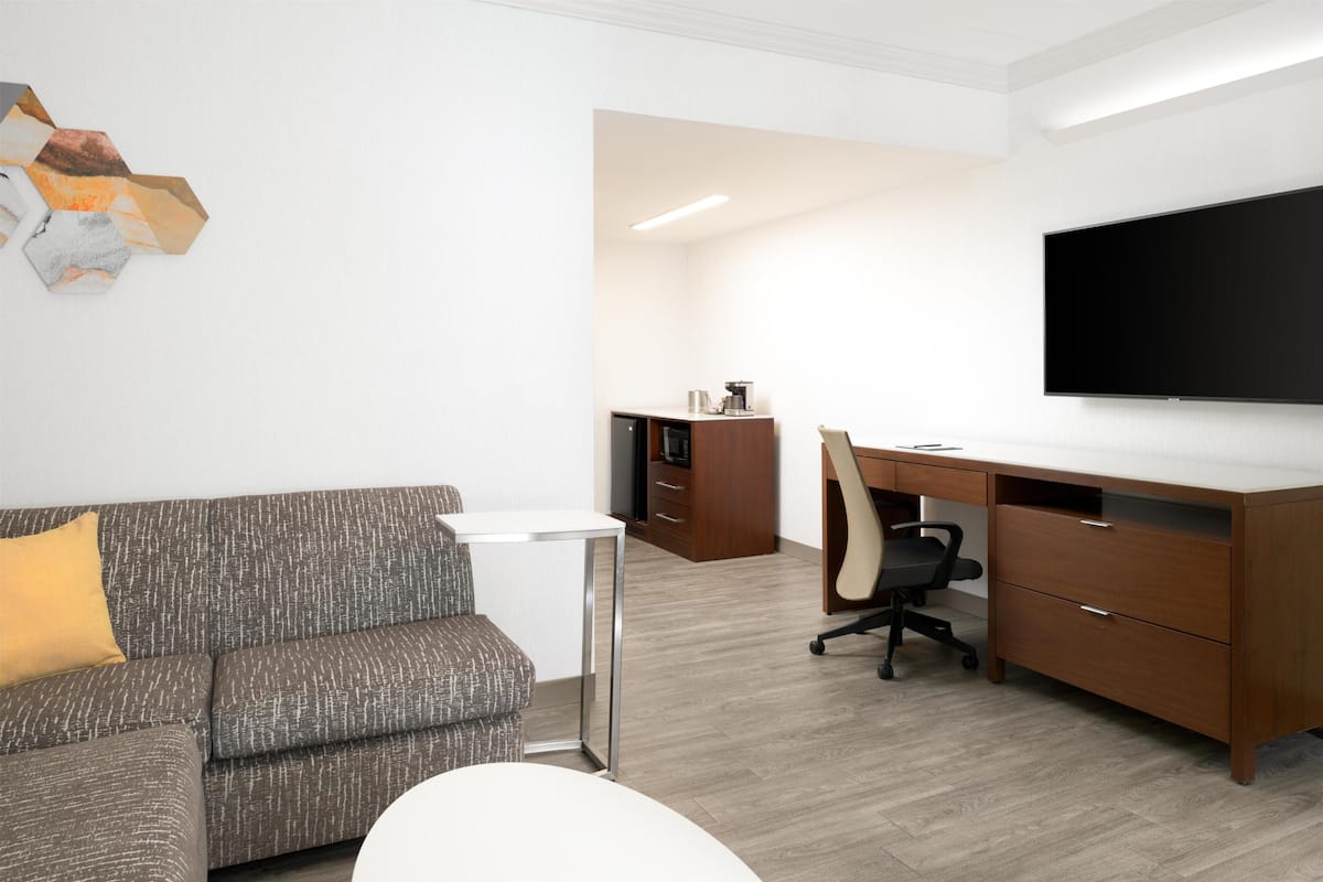 A modern office space with a sofa, desk, chair, and a flat-screen TV.