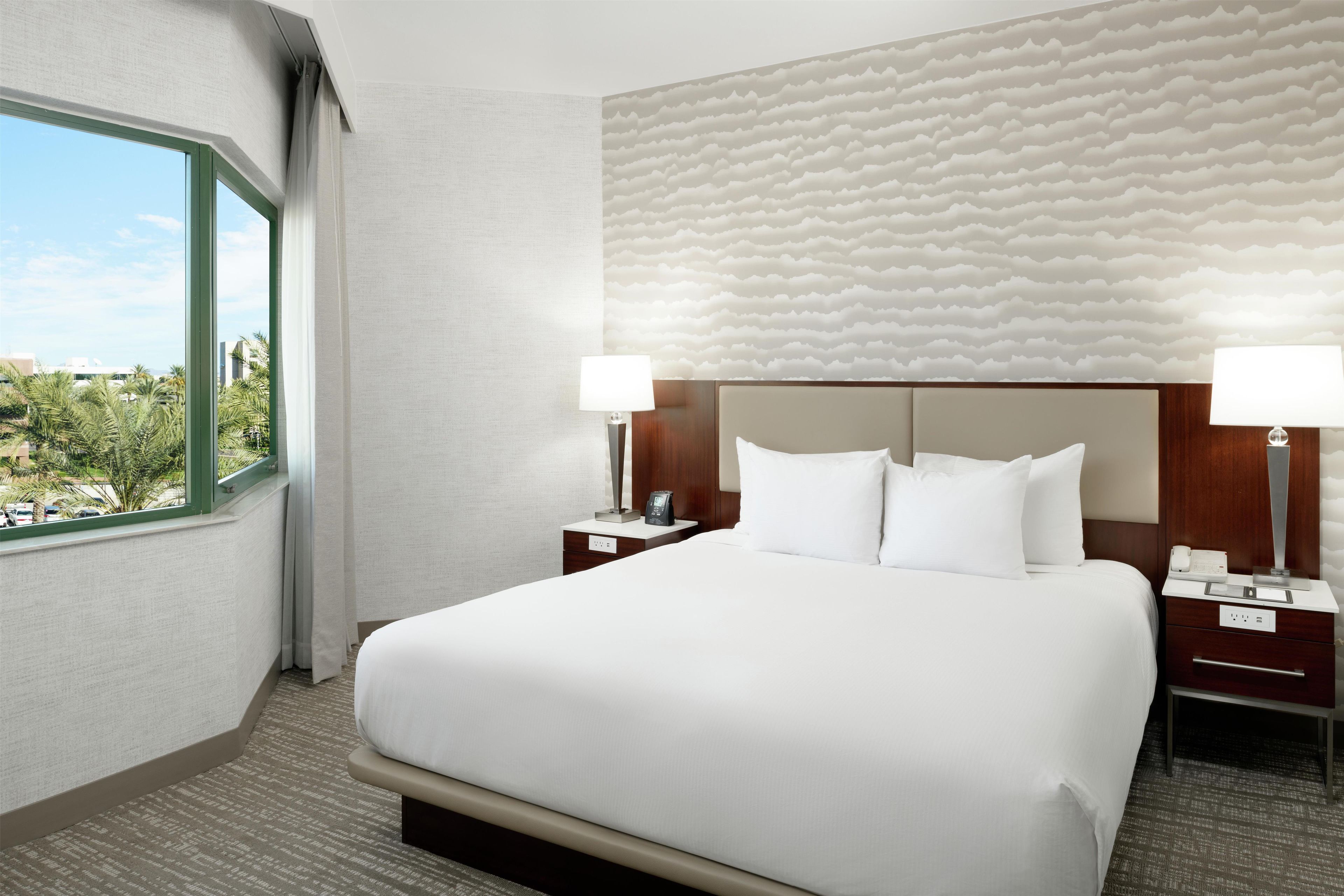 Une chambre d’hôtel avec un grand lit, deux tables de chevet, une fenêtre donnant sur un beau paysage et un mur à motifs.