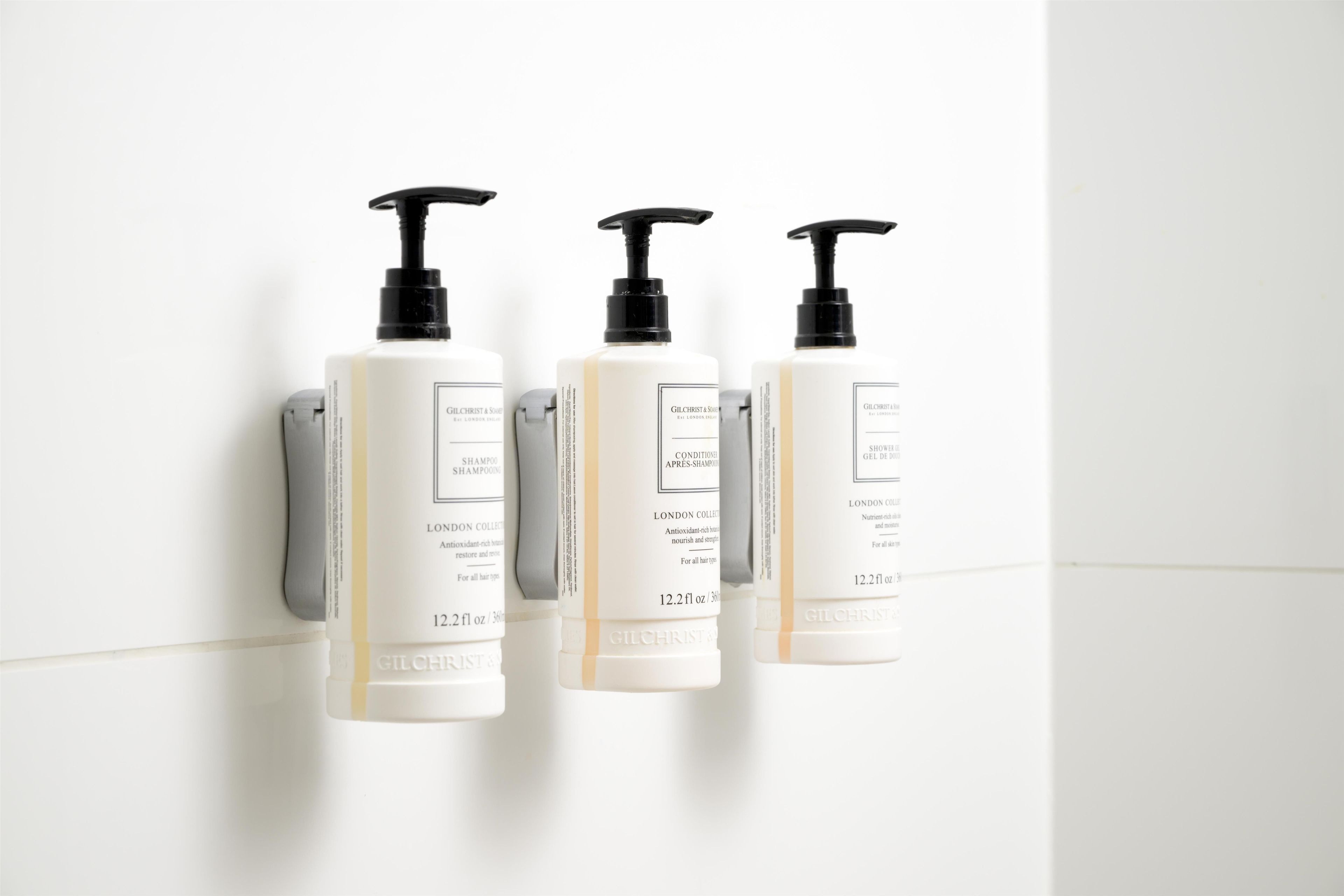 Drie flesjes shampoo van Gilchrist & Soame aan een muur bevestigd.