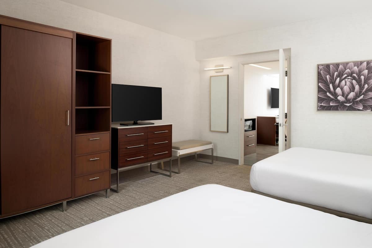 A hotel room with a large wardrobe, a desk with a chair, a television, a bed, and a mirror.