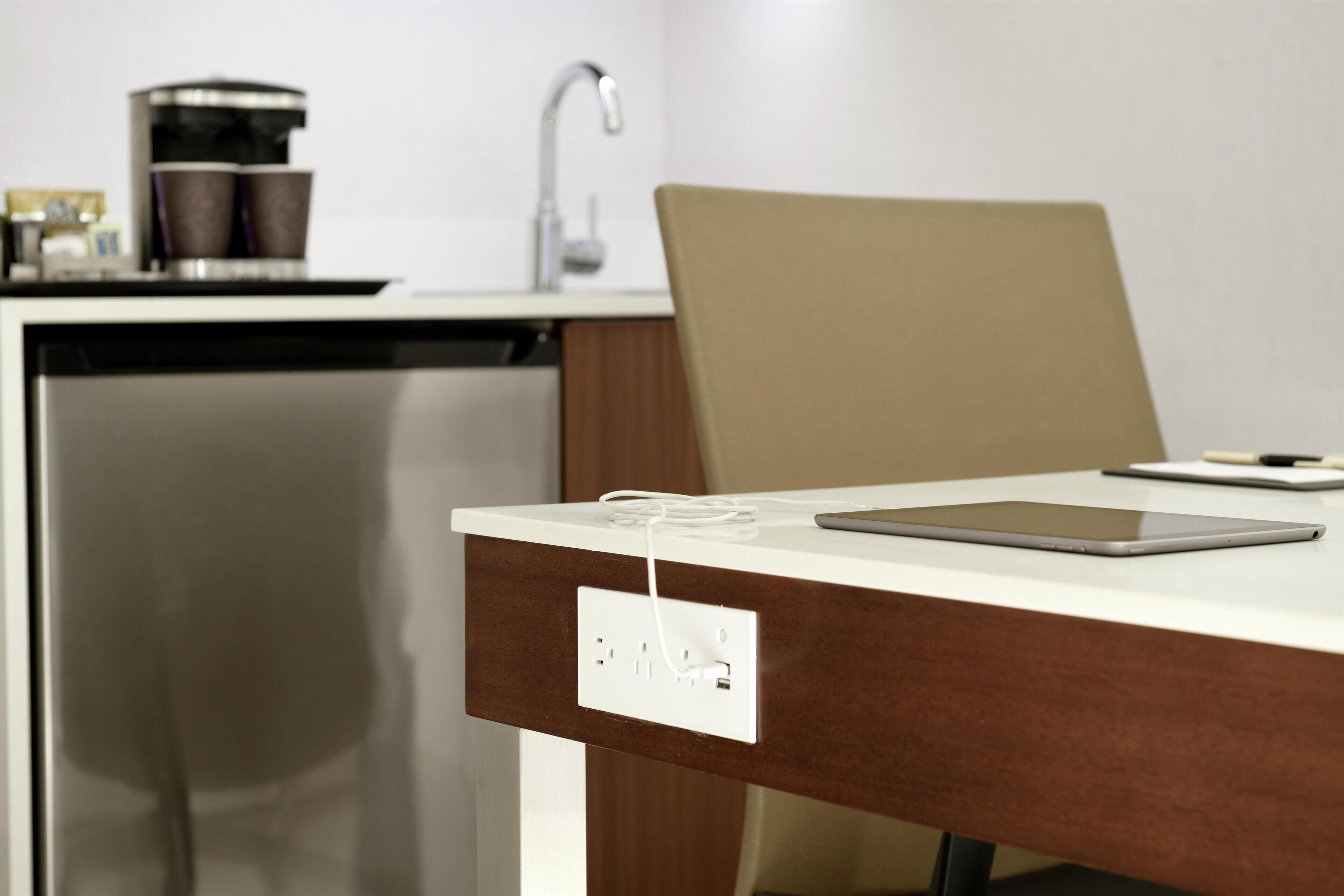 Cozinha moderna com cafeteira, pia e um tablet sobre a bancada.