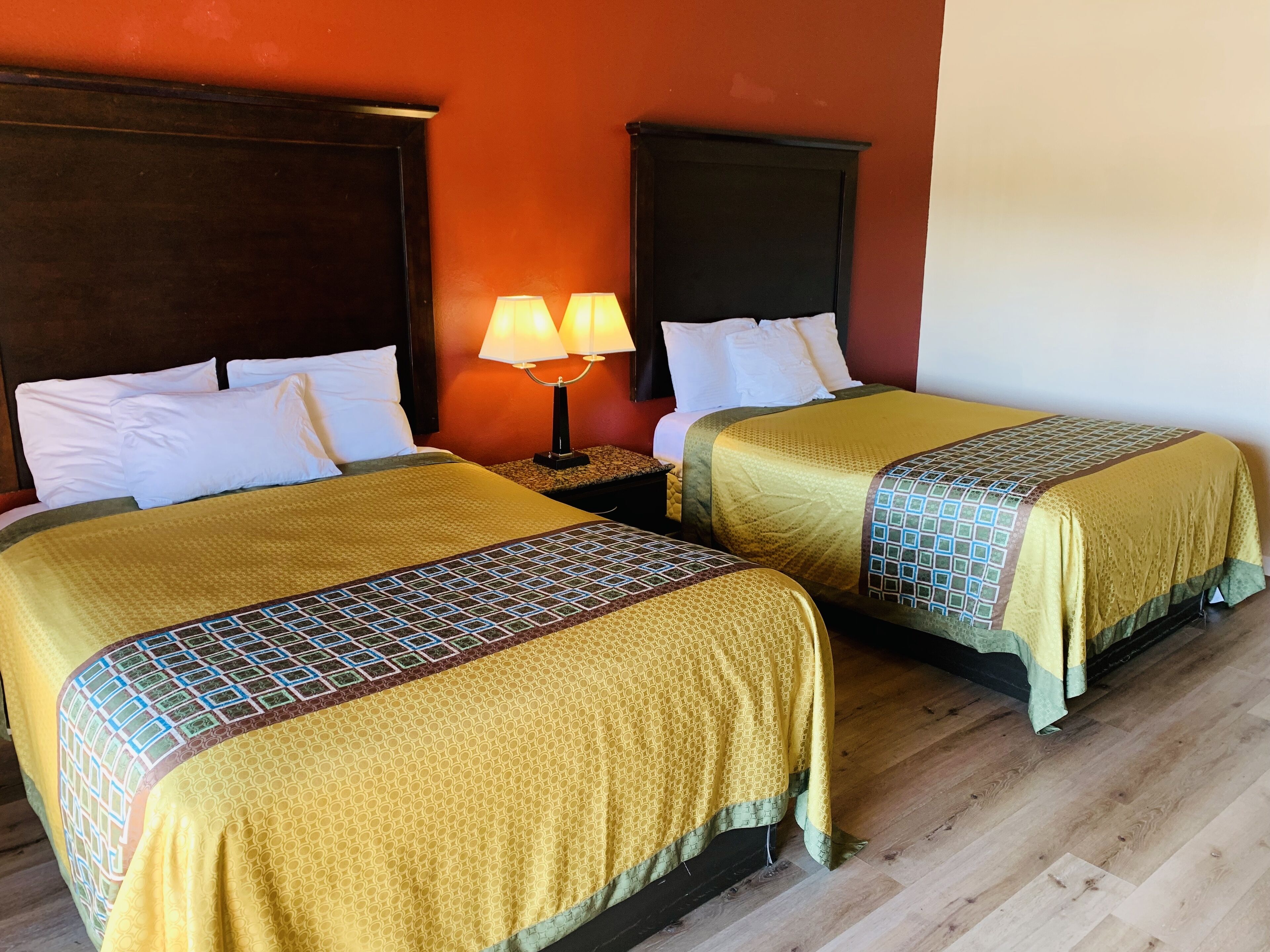 A hotel room with two beds, each with a yellow bedspread and white pillows. There is a nightstand with a lamp between the beds.