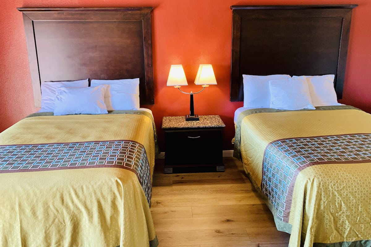 A hotel room with two beds, each with a headboard, a nightstand with a lamp, and a wooden floor.