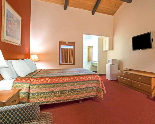 A hotel room with a bed, a TV, a desk, a chair, a dresser, and a window with curtains.