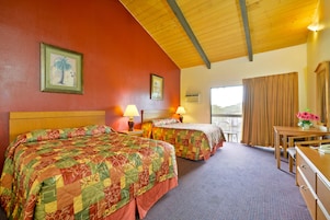Habitación de hotel con dos camas, techo de madera, balcón con vistas y escritorio con lámpara.