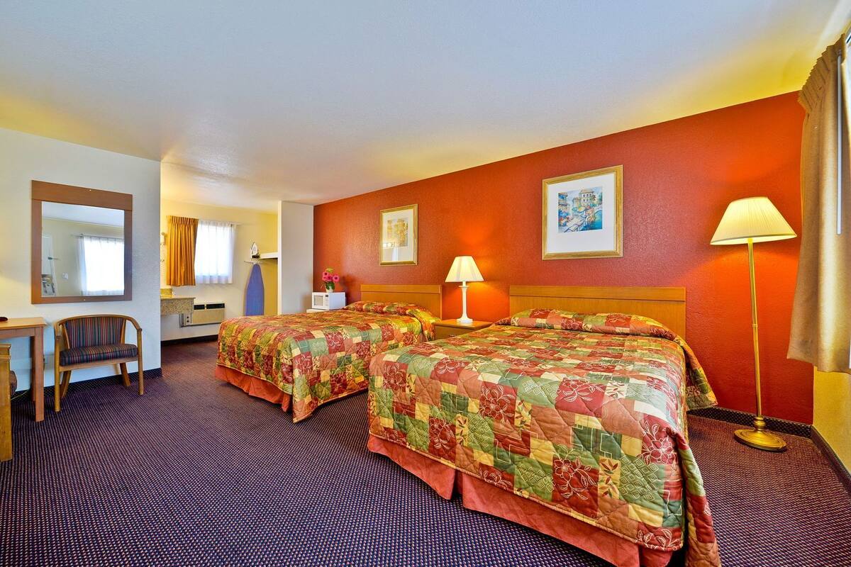 A hotel room with two beds, a desk, a chair, a lamp, and a painting on the wall.