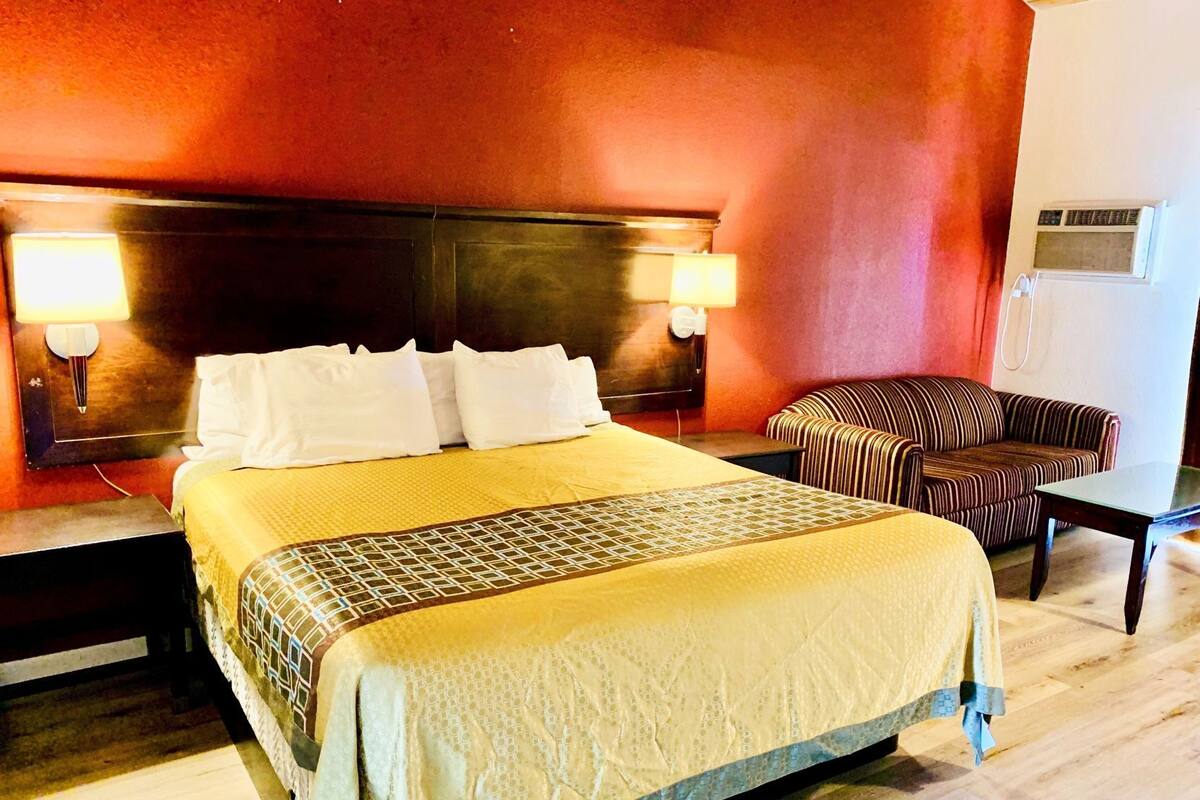 A hotel room with a large bed, two bedside lamps, a striped armchair, and a small table.