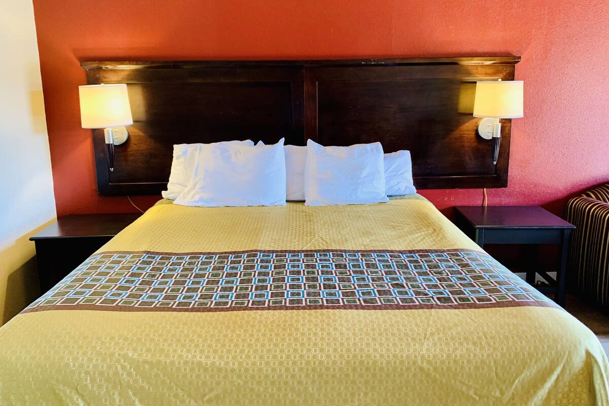 A hotel room with a large bed, two bedside tables, and a headboard with wall-mounted lamps.