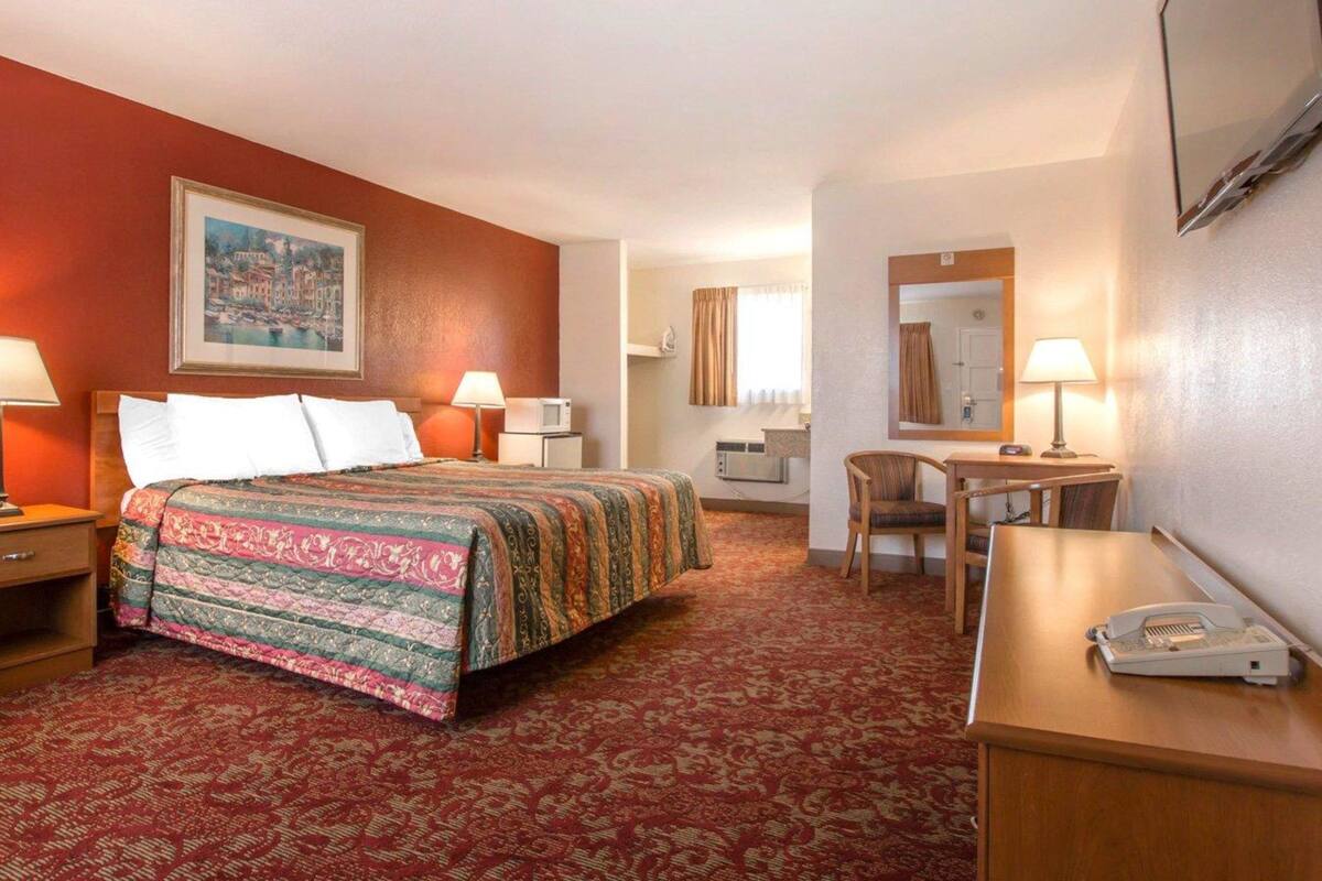 A hotel room with a bed, a desk, a chair, a telephone, and a painting on the wall.